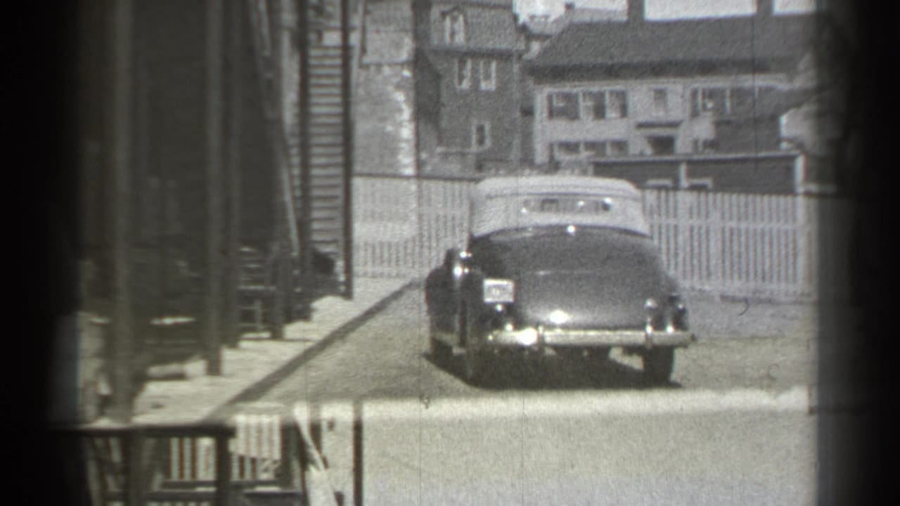 Convertible seen farther back on the street beside fences and houses.