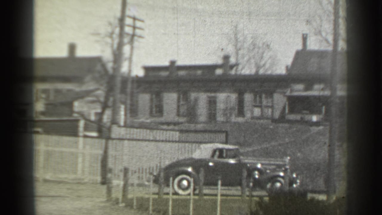 Classic car angled along the curb in front of houses and fencing.