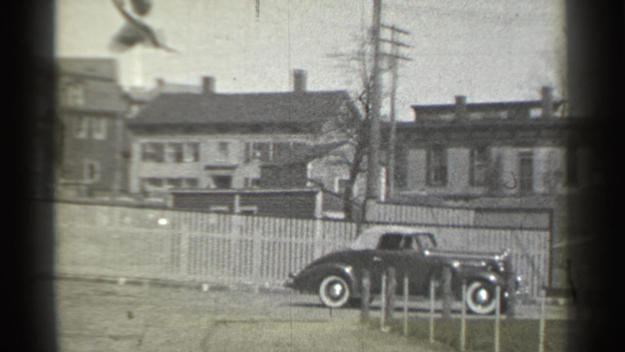 Dark vintage car beside a picket fence on a residential street.