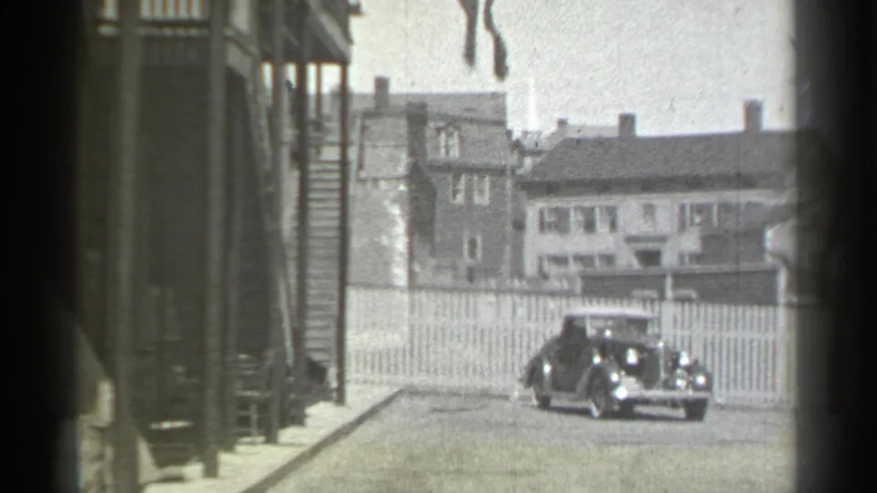 Final 1939 New York frame with the vintage car centered before a picket fence and residential houses.
