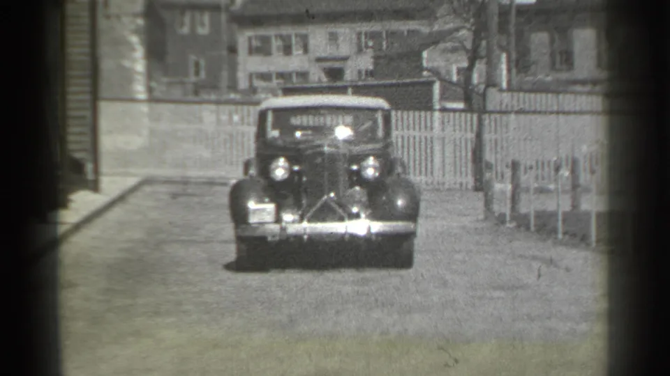 1939 New York home-movie frame of a dark convertible driving toward the camera on a quiet residential street.