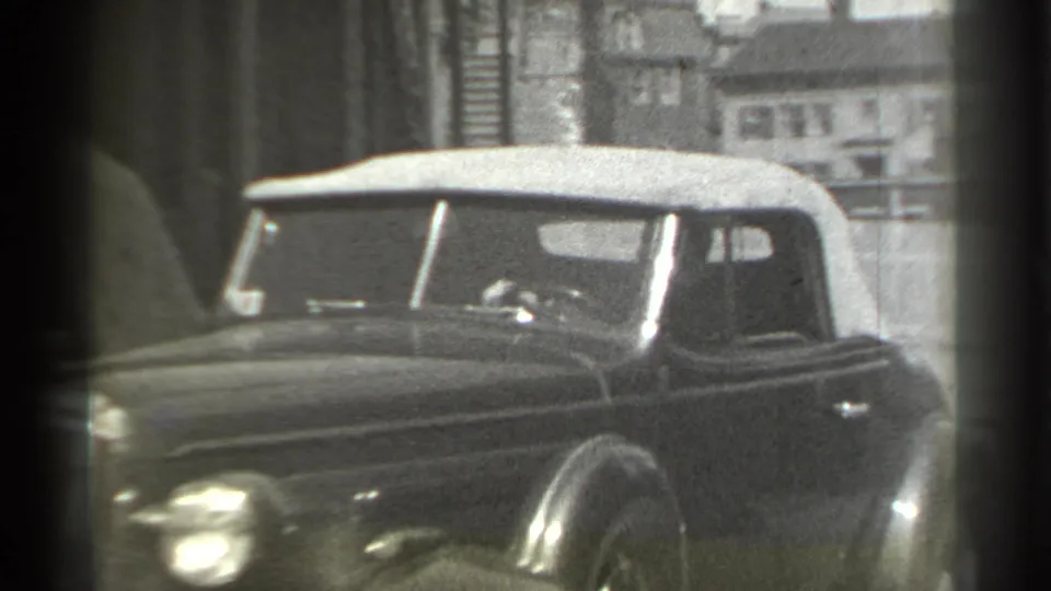 The dark convertible turns through the corner in the final 1939 New York home-movie frame, showing the side body, soft top, and street edge.