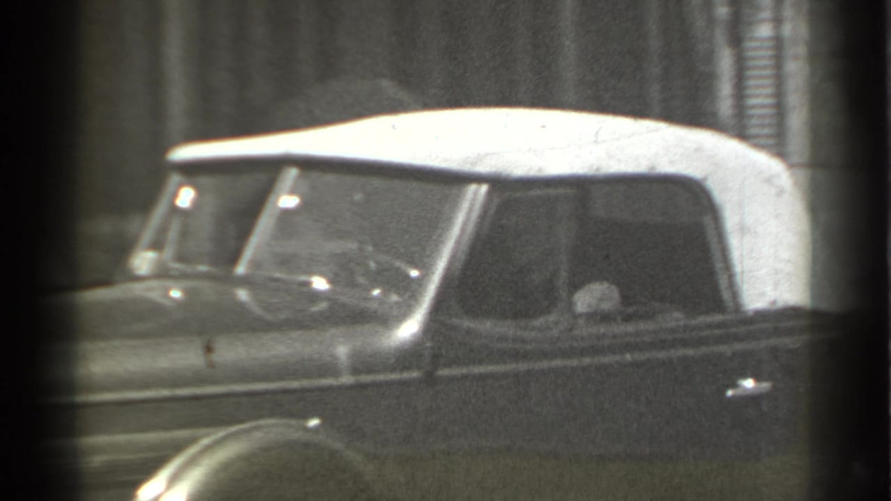 Side view of a dark 1930s convertible with a white soft top on a city street.