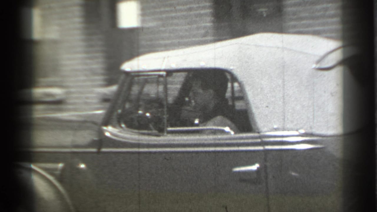 Driver visible through the side window of the convertible as it moves along the street.