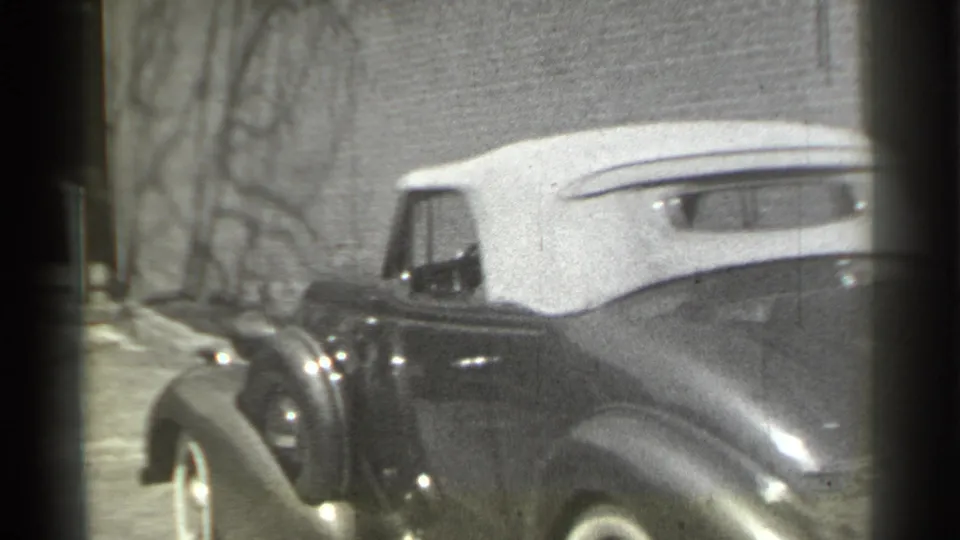 The convertible is seen from a rear three-quarter angle during its turn, showing rounded fenders, the white top, and a quiet street setting.