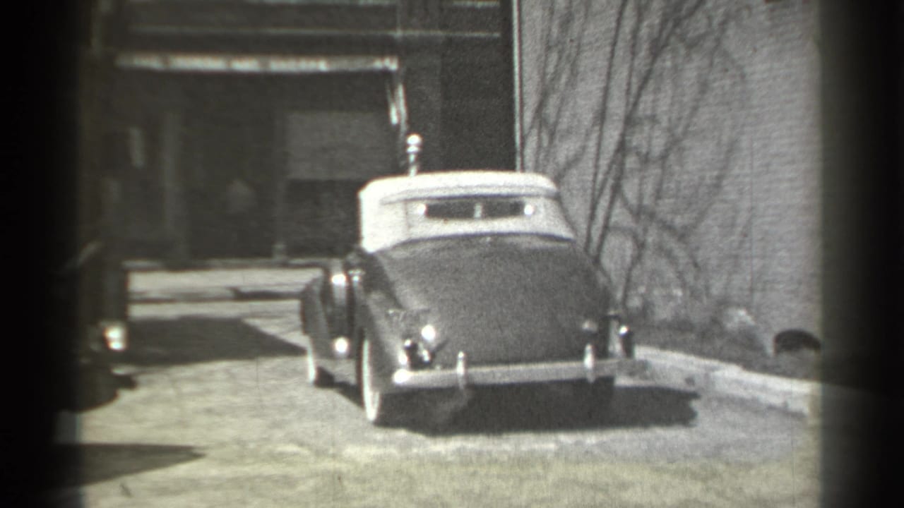 Convertible seen from the rear as it continues down the street near a doorway.