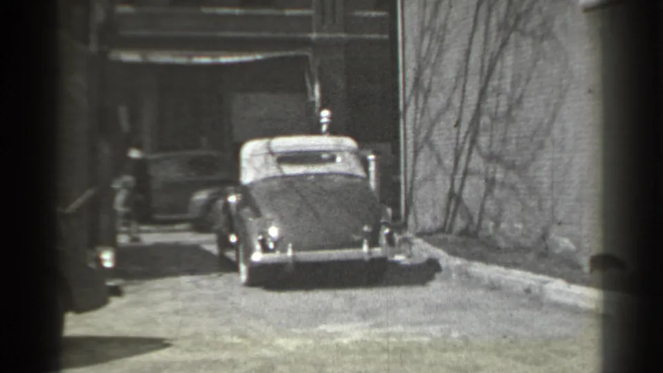 The car moves farther along the New York street, with a distant person near the building entrance in the background.