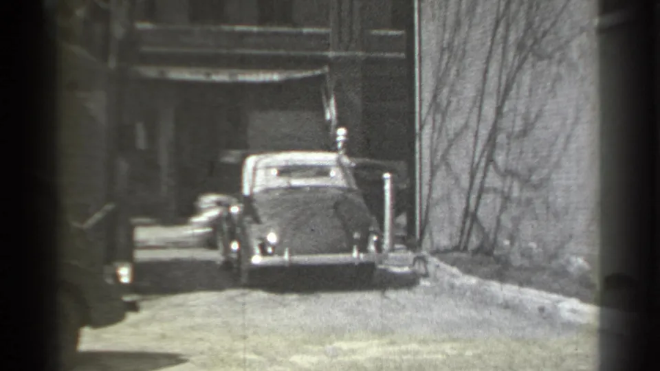 End frame of the 1939 New York street view, with the convertible receding beside the wall and bare branches.