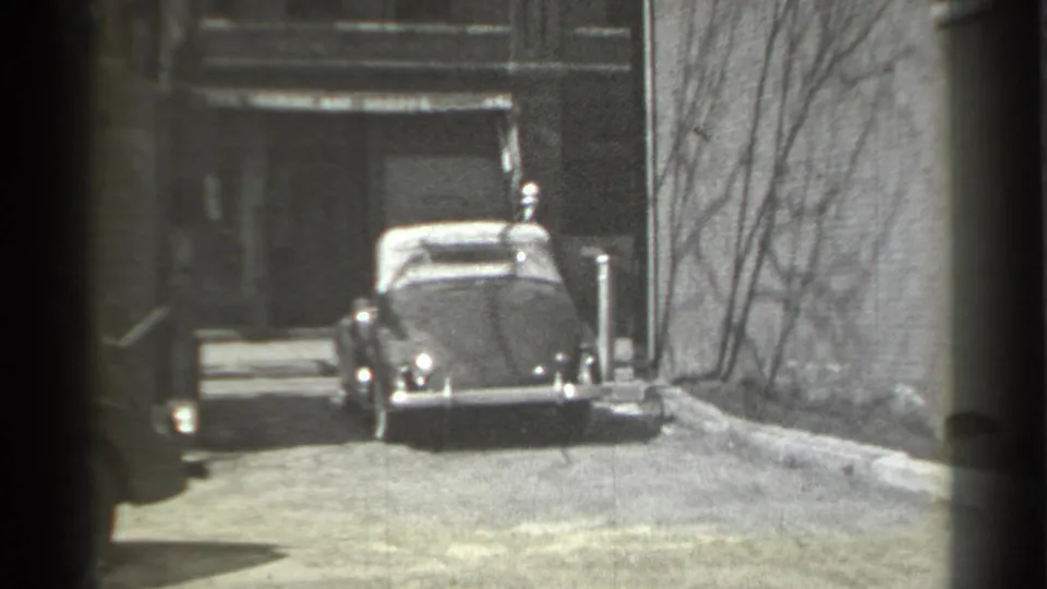1939 New York 8mm frame showing a classic convertible parked in an alley with brick walls and bare branches nearby.