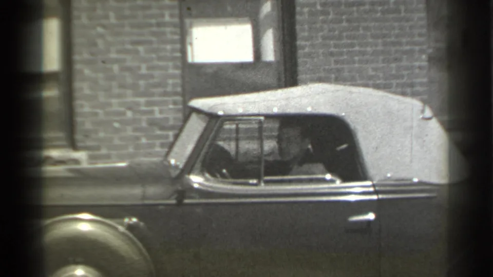 1939 New York 8mm frame showing the convertible's side, fabric roof, and a faintly visible person in the driver's seat.