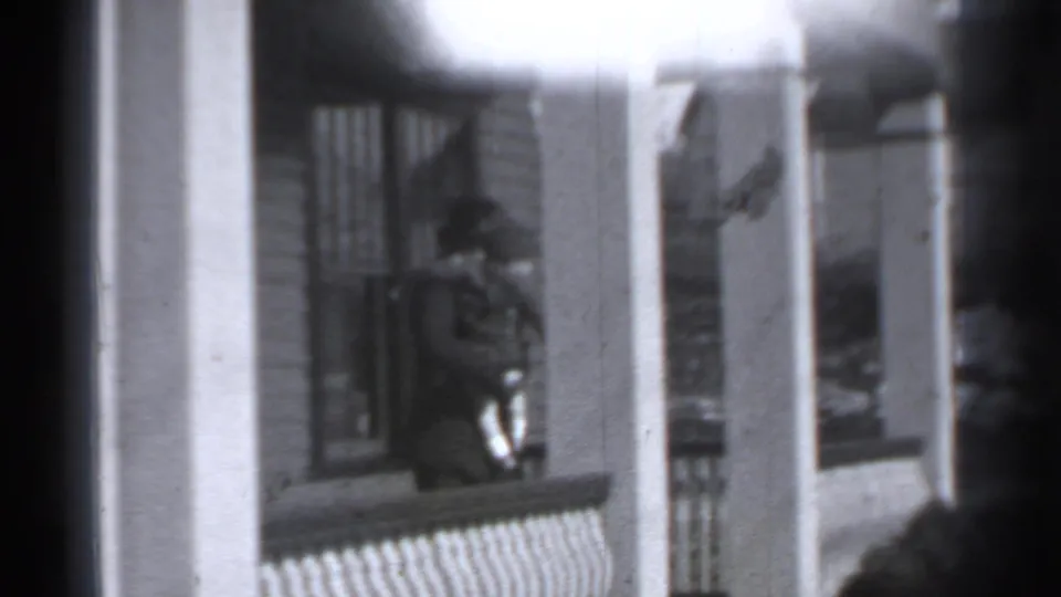 A woman in period attire carries a small child outside a New York brick building, partly obscured by soft focus and film edge shadows.