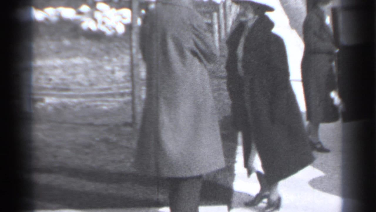 Two women in coats stand close together while another figure appears at the edge.