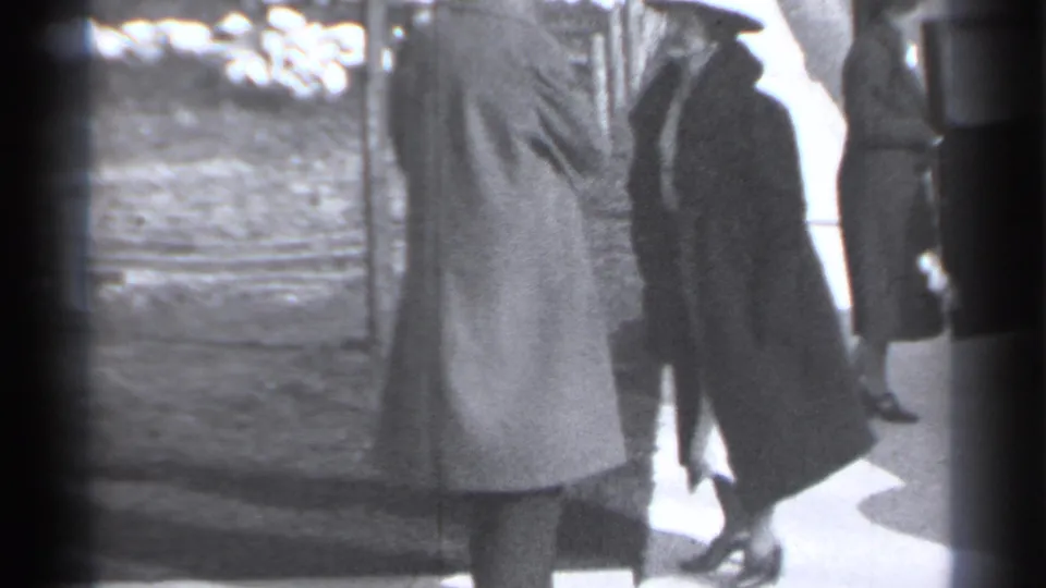 The two coated women remain near the sidewalk as a partial passerby enters the right edge of the 1939 New York frame.