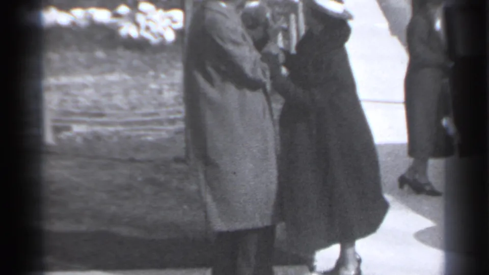 Two women in 1930s coats stand close together on a New York sidewalk while another woman walks past behind them.