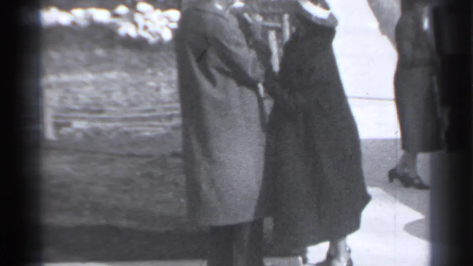 The final frame holds on the two women in coats near the sidewalk, with faces largely obscured in soft 8mm exposure.