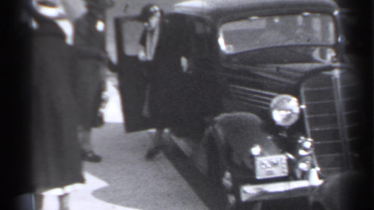 Woman in a dark coat beside a classic car on a city sidewalk.