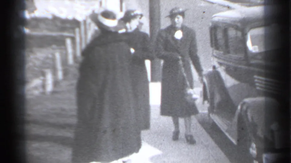 1939 New York frame with two women in dark coats and hats near a classic car as a suited man stands close by.