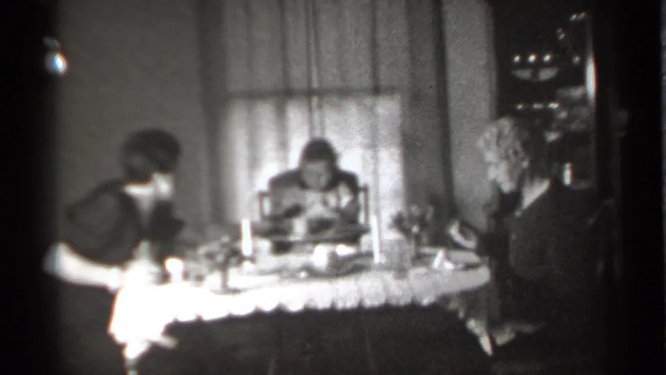 1939 New York home-movie frame showing two women and a small girl around a lace-covered dining table with cups, plates, and a candle.