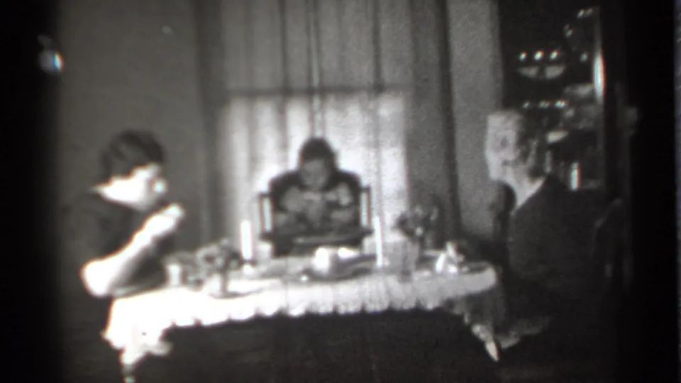 1939 New York home-movie frame with one woman raising her hand near her mouth as a child and another woman sit at the dining table.