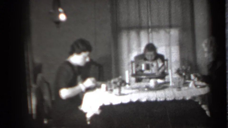 1939 New York home-movie frame showing adults at a lace-covered dining table with a child in a high chair.