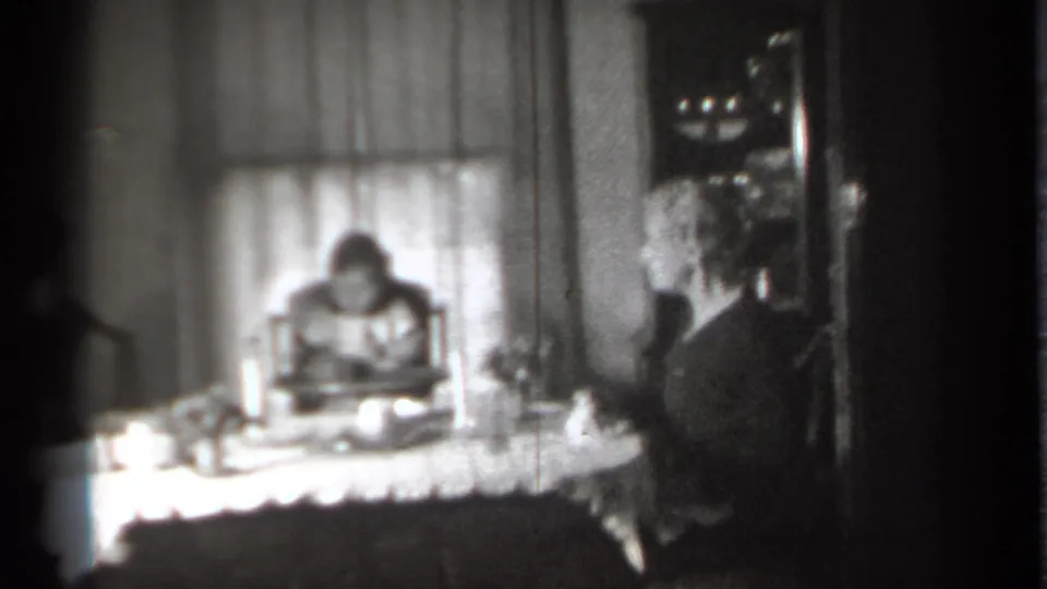 Soft 8mm frame of a New York dining room, with a child in a high chair and an adult seated beside the table.