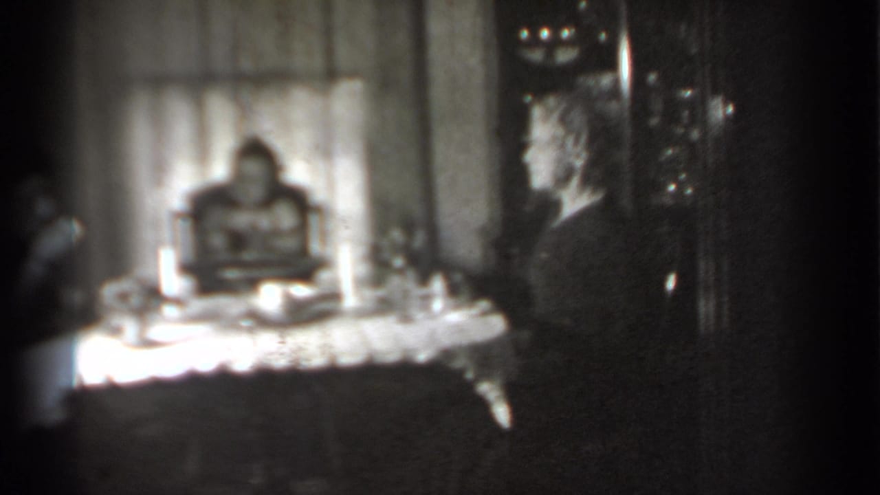 Black-and-white 1939 New York home-movie frame showing a woman in profile at a table with a baby in a high chair behind it.