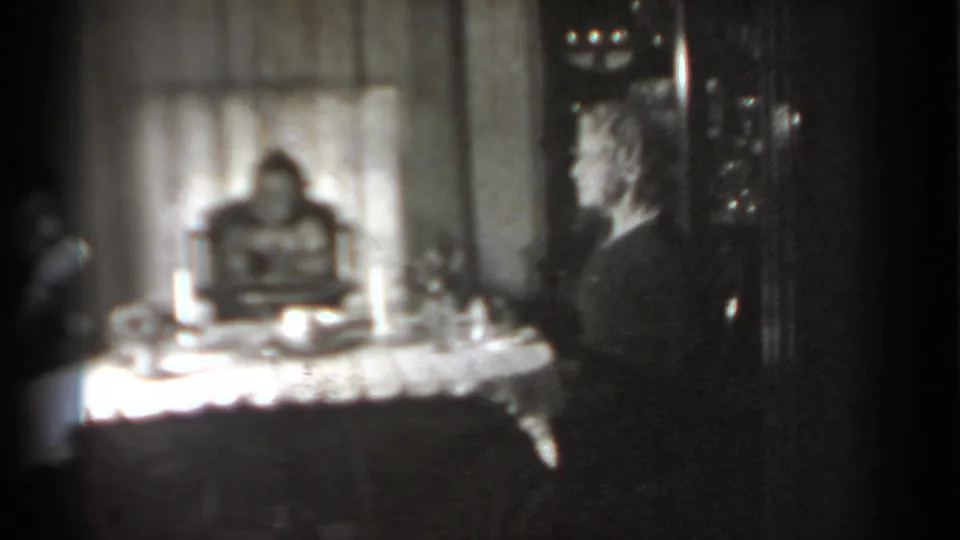 Black-and-white 1939 New York home-movie frame showing a woman in profile at a table with a baby in a high chair behind it.