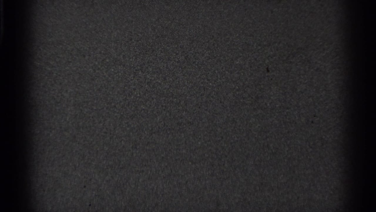Mostly blank dark film frame with visible grain and border shadow.