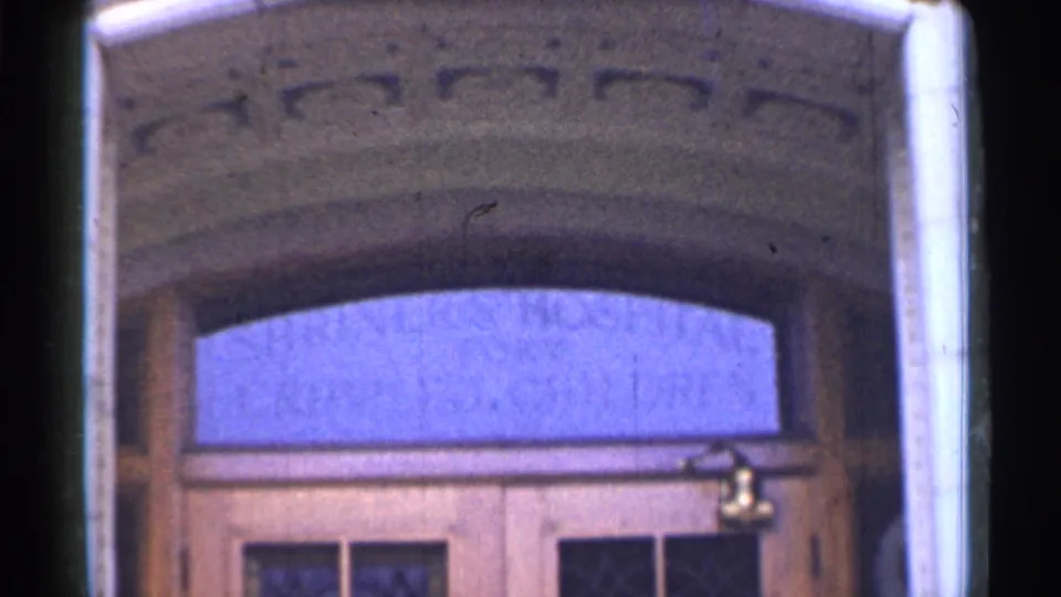Closer 1944 view of the hospital entrance, with carved arch details, blue-tinted transom glass, wooden doors, and soft 8mm color shift.