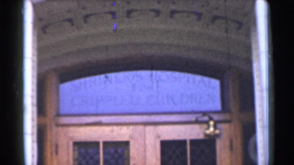 1944 San Francisco hospital doorway framed from outside, with the stone arch, blue transom, wooden doors, and visible 8mm film wear.