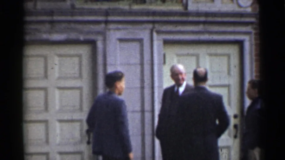 1944 San Francisco exterior frame showing several suited men conversing near paneled doors and a brick wall.