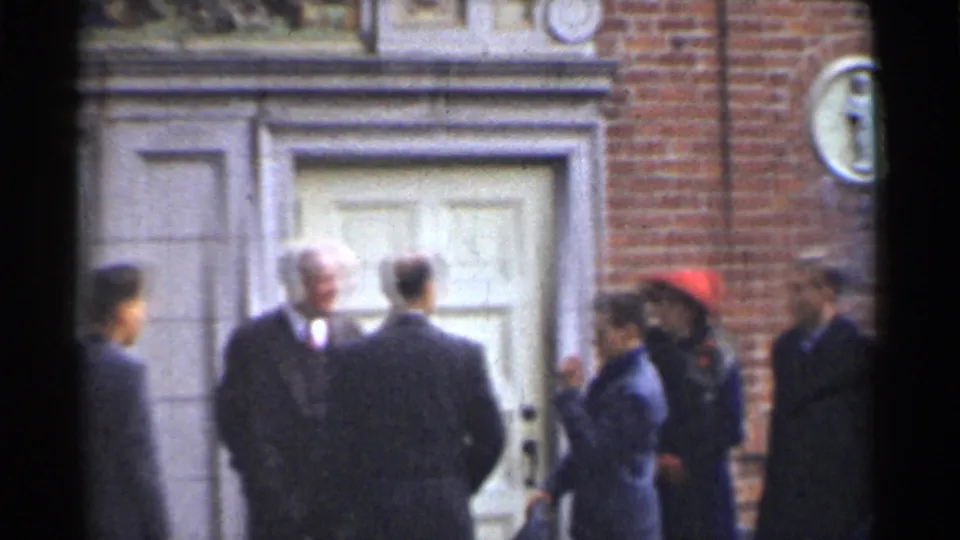 1944 San Francisco frame of men in formal suits talking outside a brick building, with a red umbrella at the edge of the group.