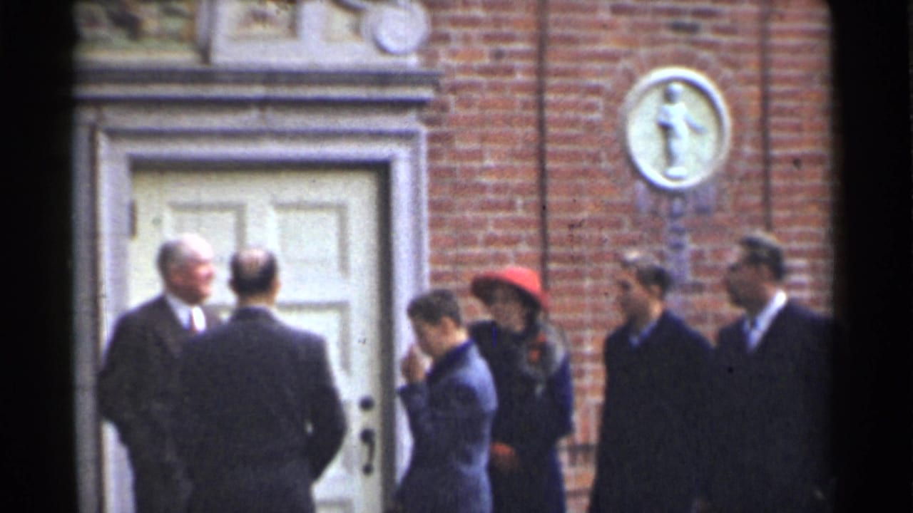1944 San Francisco home-movie frame showing adults in suits and coats talking outside a brick building entrance.