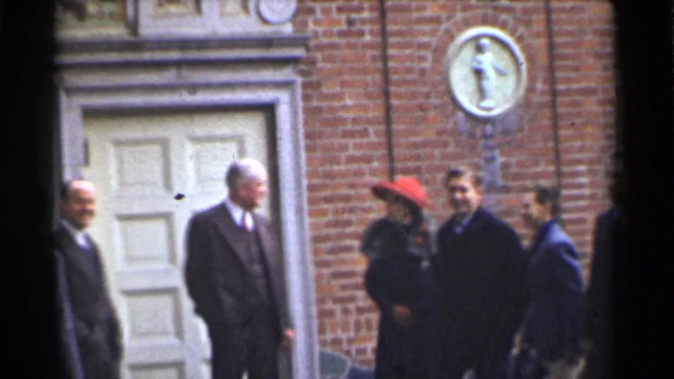 The group remains outside the San Francisco brick building, with a suited man facing others and a red-hatted woman partly visible.