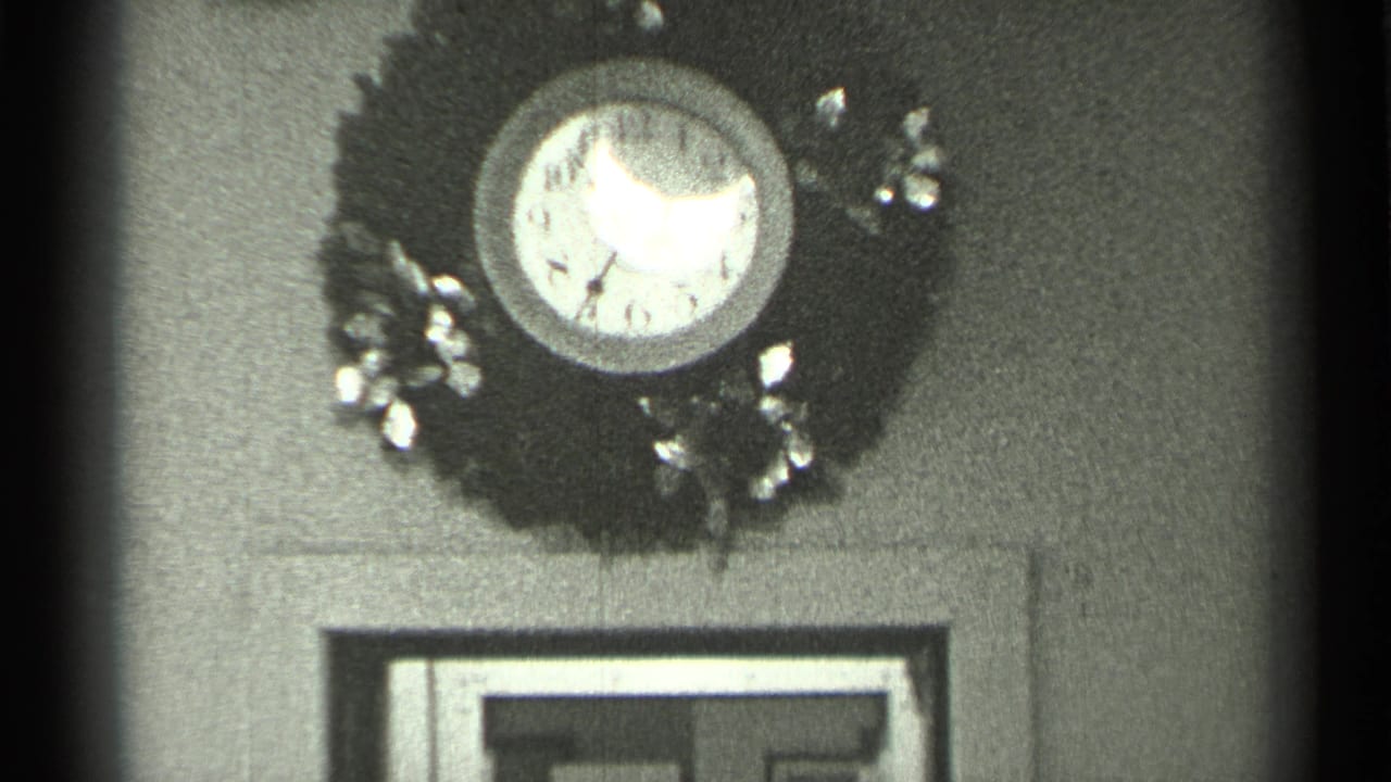 1944 San Francisco home-movie frame showing a reflective analog wall clock in a wreath above interior doorway trim.