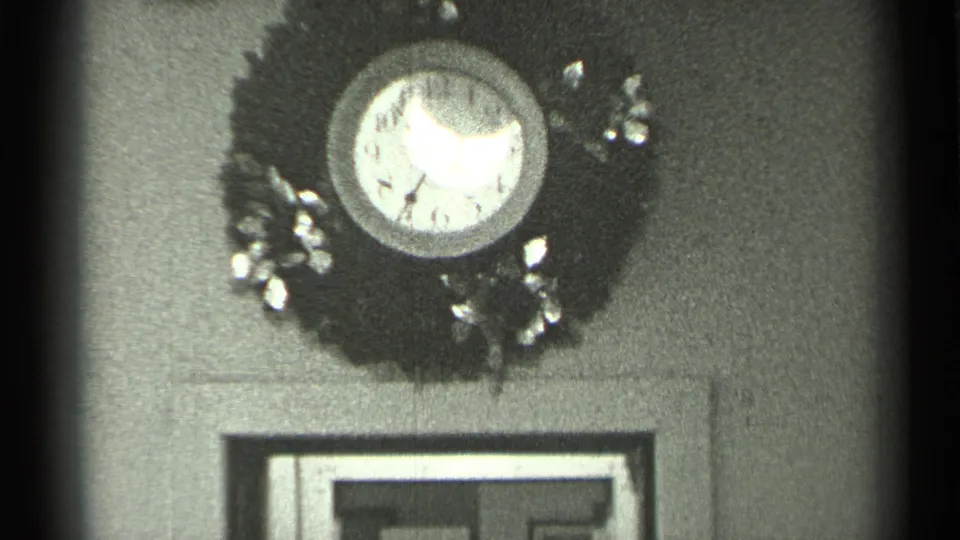1944 San Francisco home-movie frame showing a reflective analog wall clock in a wreath above interior doorway trim.