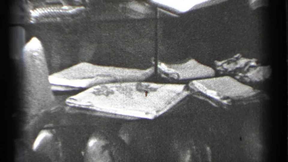 Final frame shifts to a domestic tabletop holding folded papers or cloth, with a vertical lamp or stand crossing the view.
