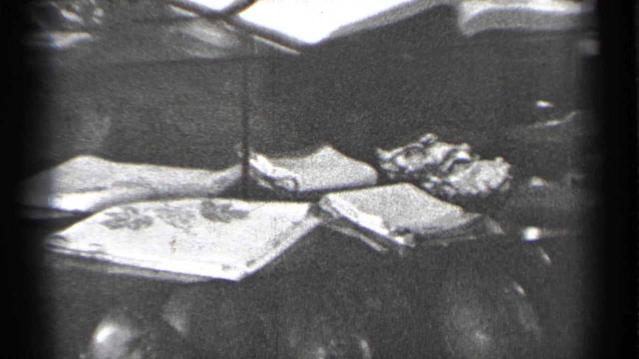 1944 San Francisco 8mm frame showing a glass case with folded fabric, small keepsakes, reflections, and a partial doll-like figure.