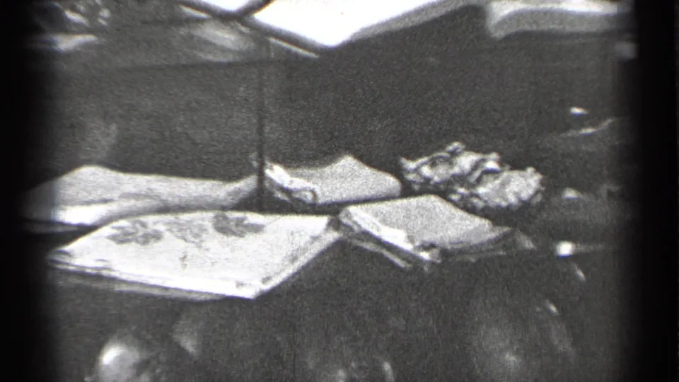 1944 San Francisco 8mm frame showing a glass case with folded fabric, small keepsakes, reflections, and a partial doll-like figure.
