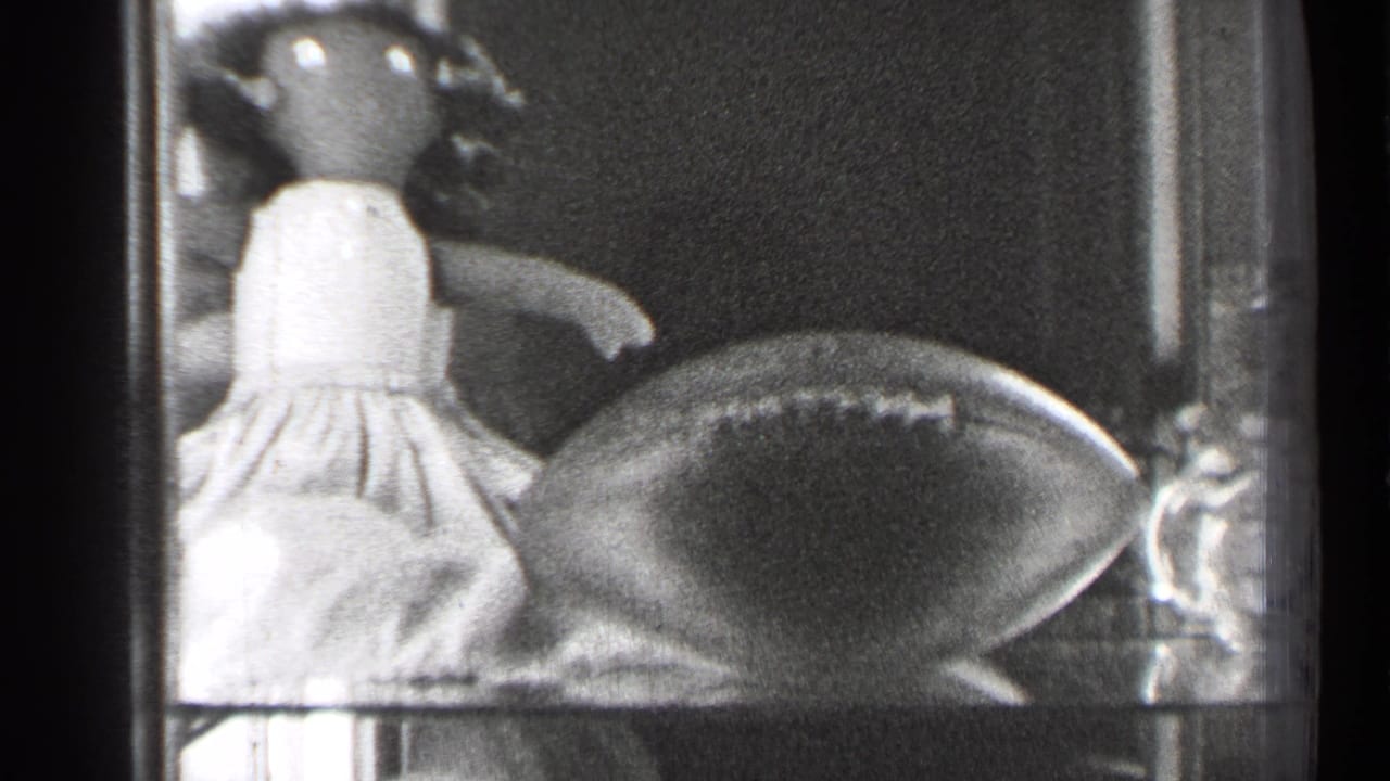 Glass display case with a doll in a light dress beside a football.