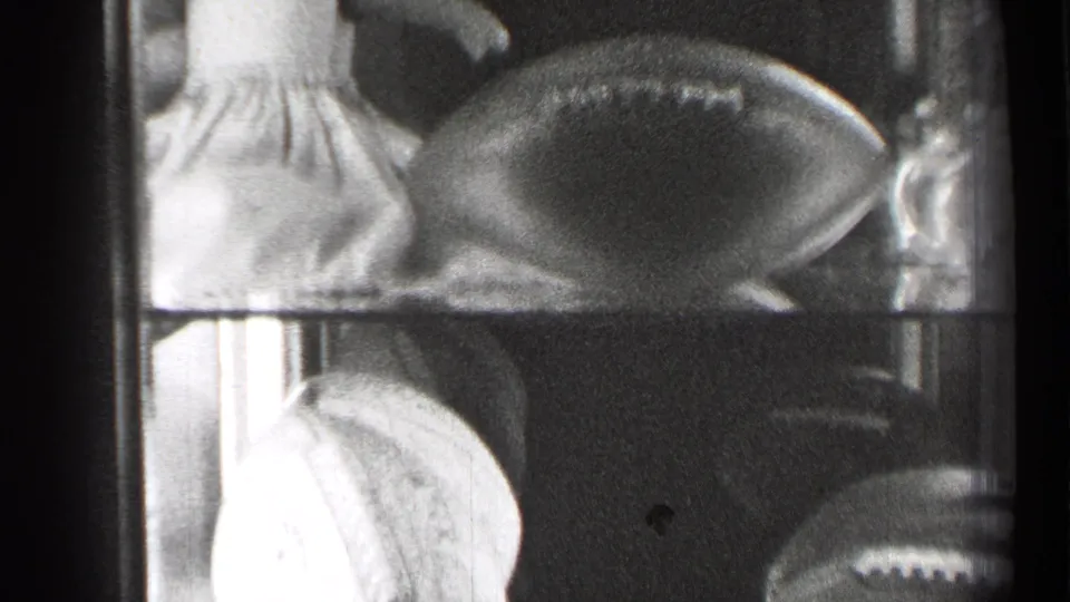 The pan reveals more of the glass case, with the doll partly cropped, a football centered, and small objects at the side.