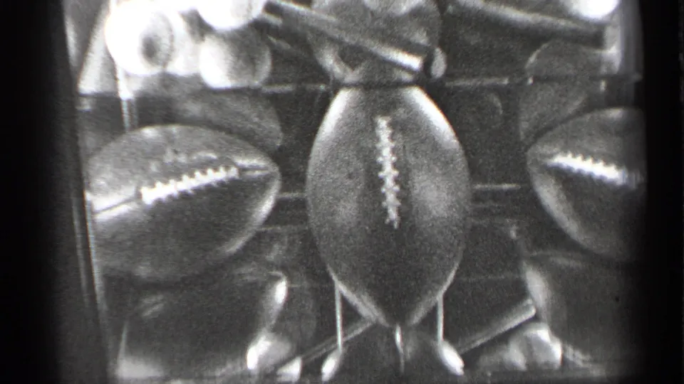 1944 black-and-white home-movie frame showing footballs beneath stacked baseballs in a glass case.