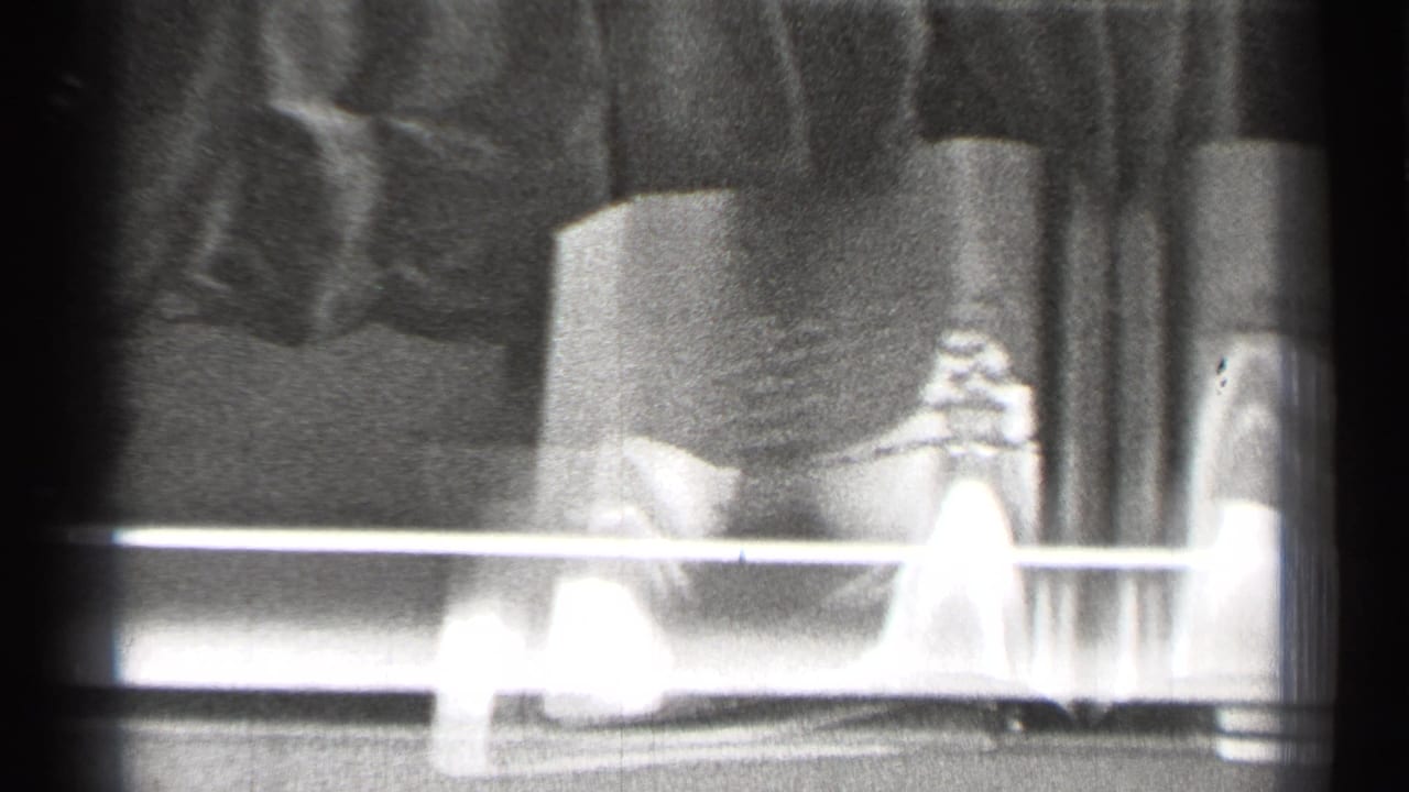 Open book behind glass with a small object on the left page and bright horizontal glare across the frame.