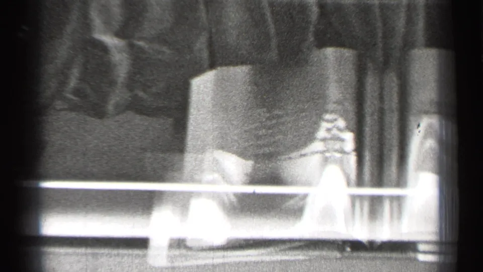 1944 San Francisco 8mm frame showing an open displayed book behind glass, with a small object on the left page and strong reflected light.