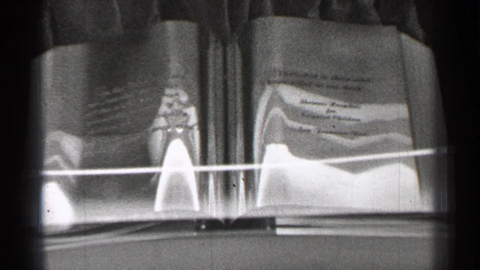 San Francisco 1944 8mm frame showing a museum-like open book display behind glass, with printed text and a small object on the page.