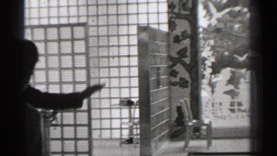 1944 San Francisco 8mm frame with a silhouetted person gesturing toward shoji-style screens and Japanese-style interior objects.