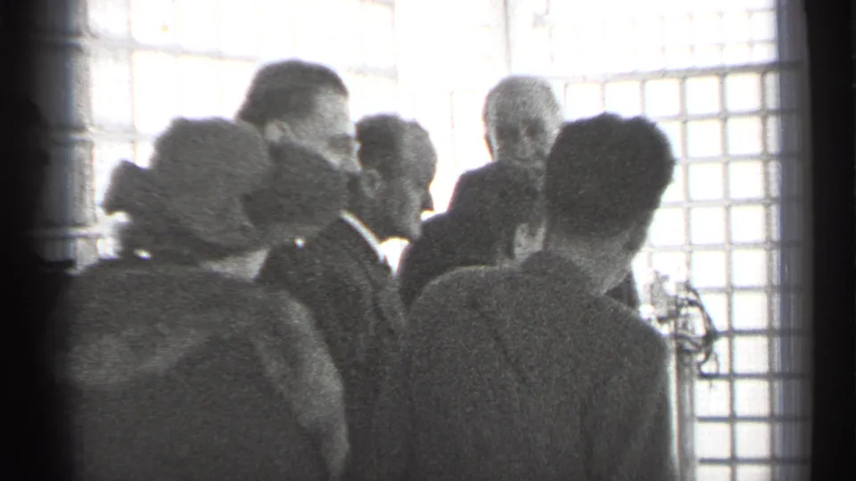 A hat-wearing woman and men in suits appear to listen inside a San Francisco office or institutional interior in 1944 home-movie footage.