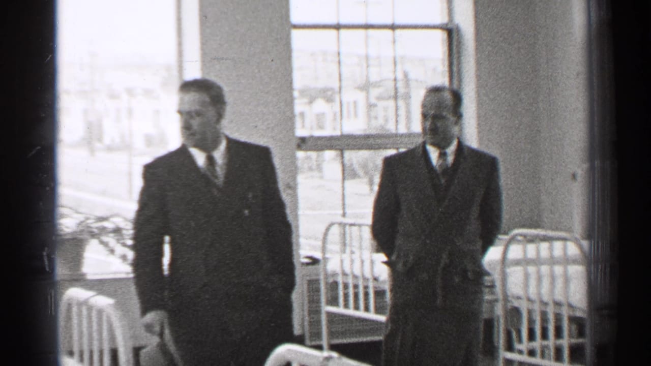 In 1944 San Francisco footage, two well-dressed men move through a hospital ward with metal beds and large windows behind them.