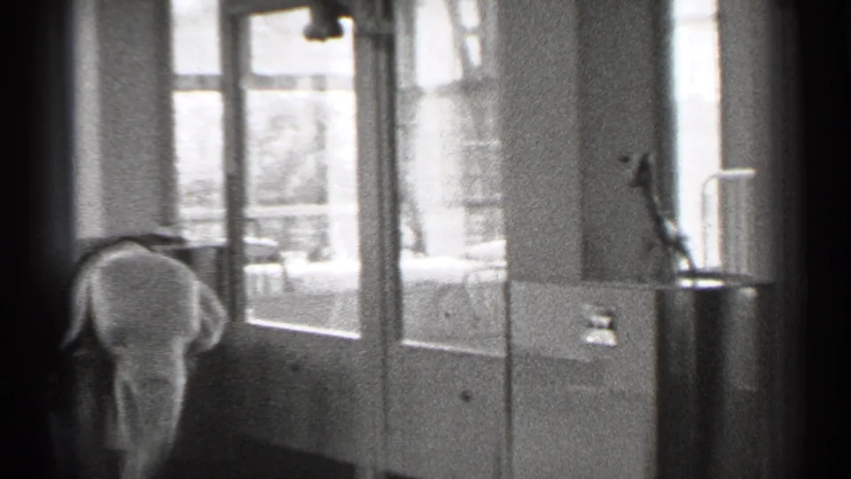 1944 San Francisco home-movie frame showing a small child or young figure near tall interior windows in a private residence.