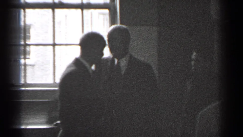 Three men in suits appear silhouetted near a large window in a dim San Francisco interior from 1944 footage.